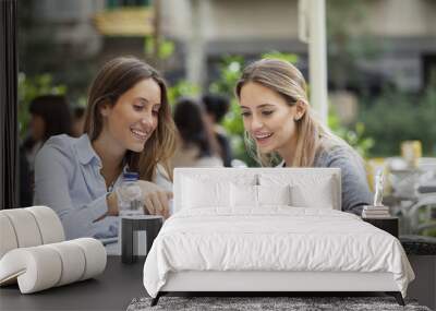 two happy friends or sisters sharing a smart phone in a coffee shop terrace looking at device Wall mural