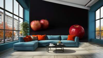 A shiny red apple isolated on black background. Two other apples out of focus in background Wall mural