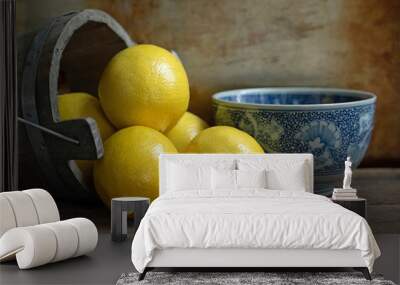 Original textured still life photograph of lemons pouring out of a wooden bucket with a blue china bowl on brown Wall mural