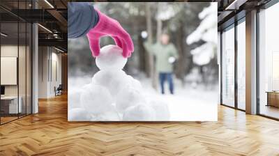 Original winter photograph of a woman's pink gloved hand picking up a snowball from a snowball pile for to have a snowball fight with man in the distance. Wall mural