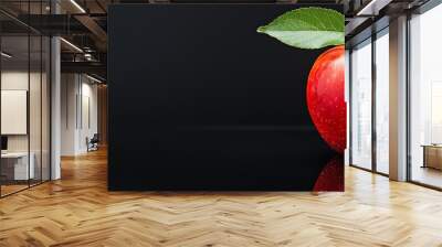  A red apple with a leaf protruding from its center on a black surface against a black backdrop Wall mural