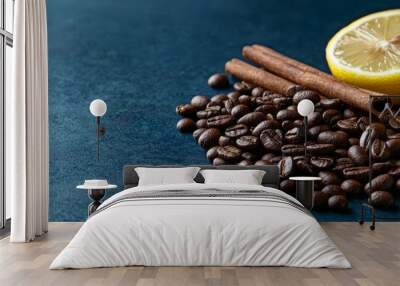  A stack of coffee beans adjacent to two lemons and cinnamon sticks against a blue backdrop on a blue surface Wall mural