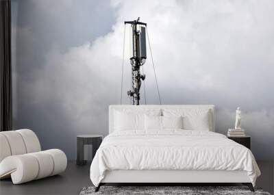 Telecomunication antenna against cloudy sky. Wall mural