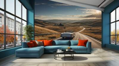 A vintage convertible car driving on a scenic road through rolling hills under a sunny sky with clouds. Wall mural