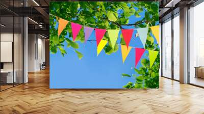 Colorful pennant string decoration against a tree and the summer sky Wall mural