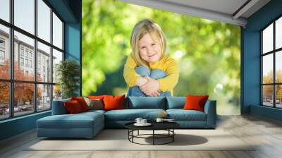 Sympathetic and beautiful little girl on a bench in a park in th Wall mural