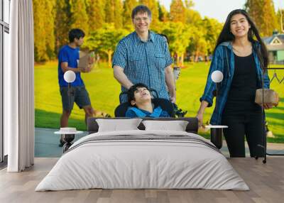 Father walking with family and disabled son at park Wall mural