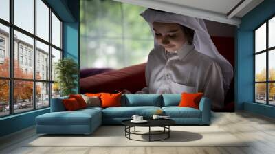 Cute Arabian kid sitting on sofa at home with tablet Wall mural