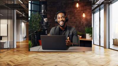  Young African American man host in headphones enjoying podcasting in his home studio. Handsome podcaster laughing while streaming live audio podcast

 Wall mural