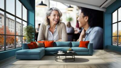 Happy smiling middle aged female friends sitting in a café laughing and talking during a lunch break Wall mural