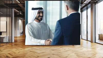 International operations manager meeting Muslim business partner in traditional white Kandura. They're standing in office, shaking hands. Wall mural