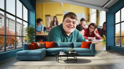 Portrait of a young smiling man with Down syndrome in the classroom with his classmates. Social integration concept. Wall mural