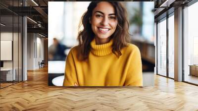 Portrait of beautiful happy woman in yellow sweater looking at camera in the office, blurred people in background Wall mural