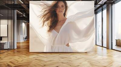 Woman in a long white dress walking in the desert with flowing fabric in the wind Wall mural