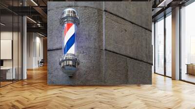 A classic barber pole with illuminated red, white and blue stripes, mounted on a stone wall on a street in Barcelona in Catalonia Spain Wall mural