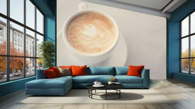 Cup of coffee with milk on marble table with wooden chairs in unfocused background, top view Wall mural