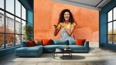 Black woman laughing and listening to music with earphones. Wall mural