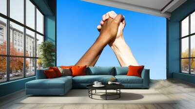 Multiethnic women's hands together against blue sky. Wall mural