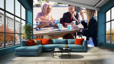 Positive diverse women having coffee break at table in park Wall mural