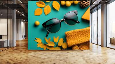 Stylish autumn flat lay with sunglasses, sweater, leaves, and accessories on a teal background. Wall mural