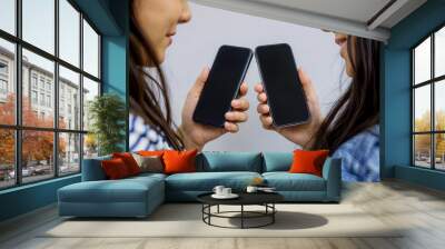 Two girls holding mobile smart phone next to each other sharing mockup white screen background clipping using smartphones blank working or looking on cellphone unrecognizable close up top view above
 Wall mural