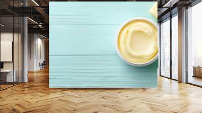 Smooth butter in a bowl with a piece on a light green wooden surface, perfect for culinary or baking themes. Wall mural