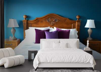 A bedroom with a blue wall and a white bed with a wooden headboard. The bed is made with white sheets and has violet pillows. There are two nightstands on either side of the bed, both with a lamp Wall mural