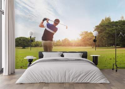 Golfer hitting golf shot with club on course at evening time. Wall mural