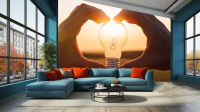 A light bulb held by two fingers with the sunset shining through it against a white background, symbolizing innovation and creativity Wall mural