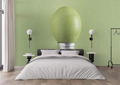 Delicate olive green Easter egg as bulb isolated on pale green background creative idea. Minimal flat lay. Wall mural