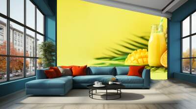 Delicious juicy smoothie with orange fruit, mango, pineapple on yellow background. Copy space. Pop art design, creative summer concept. Fresh juice in glass jar over green palm leaves. Banner Wall mural