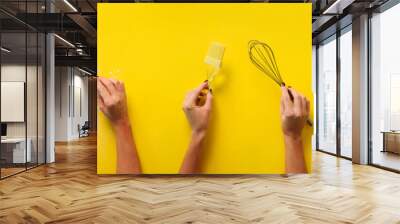 Female hands holding kitchen tools, sieve, rolling pin, bowl, sieve, brush, whisk, spatula for baking and cooking over yellow background. Food frame, bake concept with copy space Wall mural