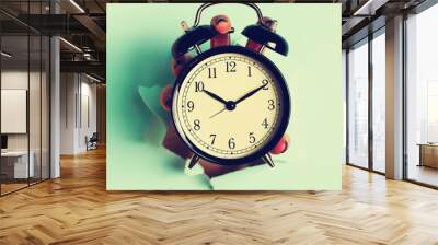 Hand holding black alarm clock through hole in blue paper background. Wake up alert concept. Square crop. Morning routine Wall mural