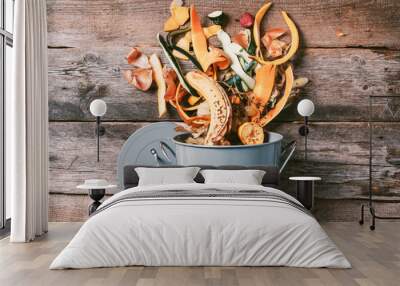 Peeled vegetables on chopping board, white compost bin on wooden background. Top view of kitchen food waste collected in recycling compost pot. Wall mural