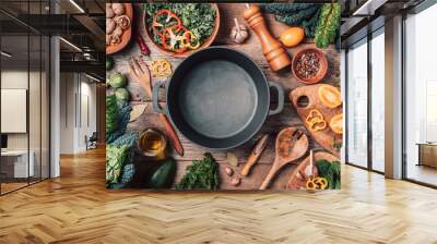 Various organic vegetables ingredients and empty iron cooking pot, wooden bowls, spoons on wooden background. Top view, copy space. Organic vegetables ingredients for vegan cooking. Clean eating food Wall mural