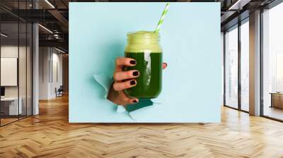 Woman hand holding glass jar of green smoothie, fresh juice against blue background. Healthy beverage, vegan, vegetarian concept. Banner with copy space Wall mural