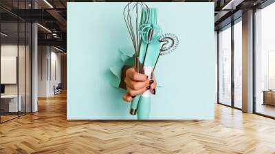 Woman hand holding kitchen utensils on blue background. Baking tools - brush, whisk, spatula. Bakery, cooking, healthy homemade food concept. Copy space Wall mural