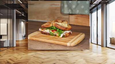 Satisfied tasty sandwich made from white bread, prague ham, slices of gouda cheese, sunny side up egg and green rocket leaves and served as a main course for the lunch or dinner on the wooden board. Wall mural