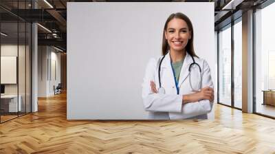 Cheerful young female doctor with a confident smile standing in a white studio background. Wall mural