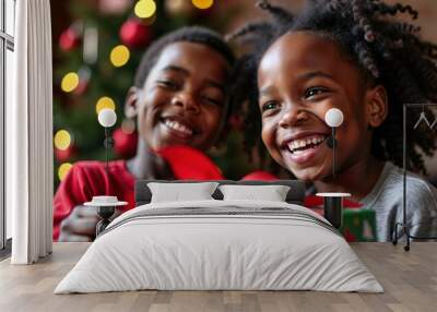 Portrait of two young African American children unwrapping a Christmas gift against a Christmas background. They are laughing and smiling and extremely happy and excited. Wall mural