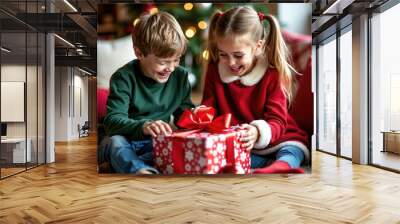 Portrait of two young children unwrapping a Christmas gift against a Christmas background. They are laughing, and smiling and extremely happy and excited. Wall mural