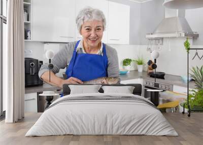 Happy senior woman in the kitchen preparing fresh fish. Wall mural