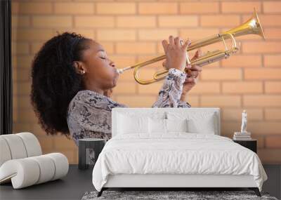 Young afro american woman playing the trumpet with her eyes closed on a brick wall background Wall mural