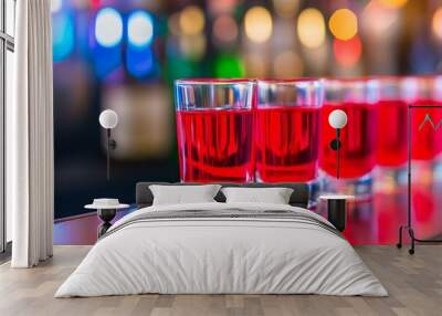 Row of red drinks in shot glasses standing on bar with neon lights reflecting Wall mural