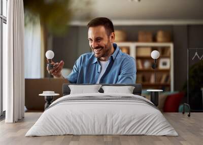 A cheerful adult male online teacher talking with his students on an online platform for his online class on his laptop. Wall mural