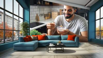 Attractive bearded man sitting at his nice kitchen table, eating cereals for breakfast Wall mural