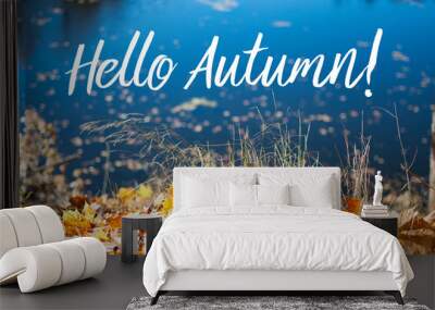 Beautiful autumn landscape with maple foliage on the ground in the front, on the dark blue river background. Colorful wallpaper with white Hello Autumn text Wall mural