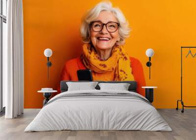 charismatic elderly woman laughing with smartphone vibrant orange background joyful expression modern senior lifestyle Wall mural