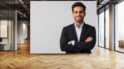 charismatic indian businessman in smart casual attire confident pose with folded hands against clean white backdrop warm smile conveys approachability and professionalism modern corporate portrait Wall mural