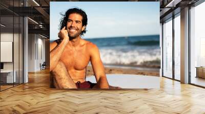 Handsome man talking to the phone. Surfer taking a break on the beach. Wall mural